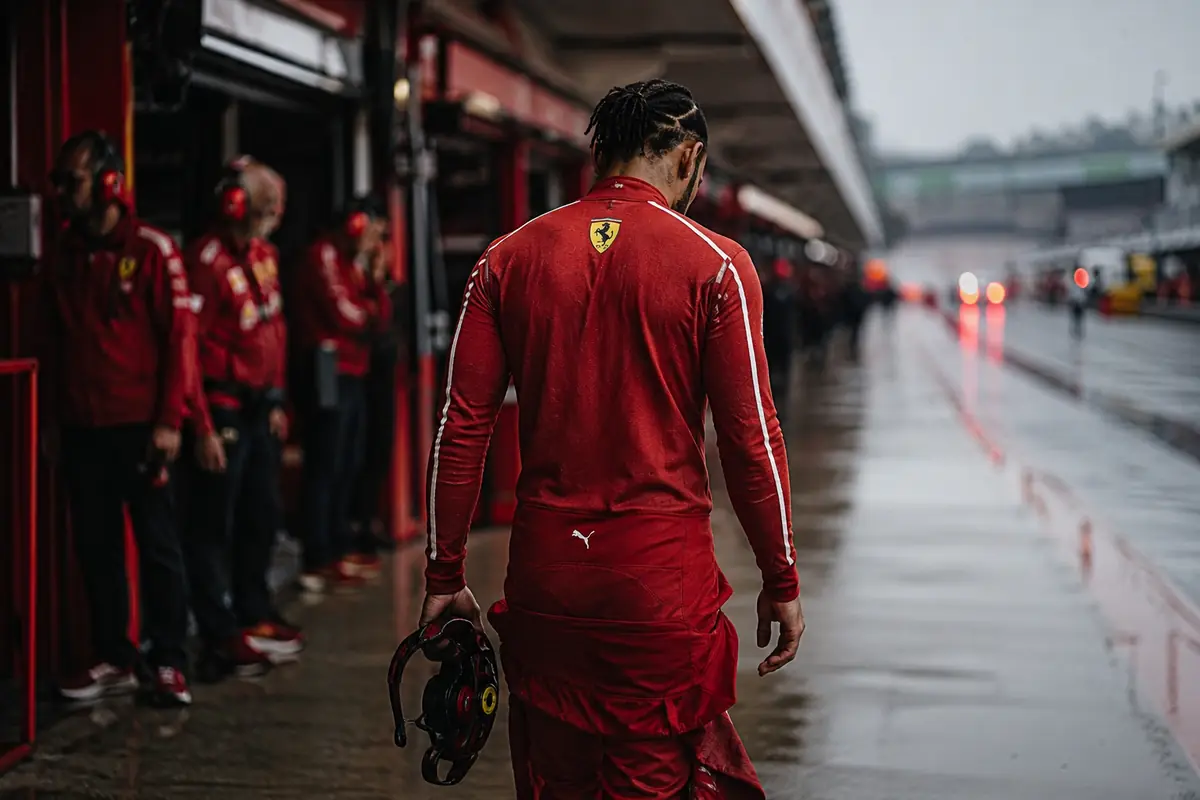 Hamilton con la tuta della Ferrari a testa bassa davanti al box